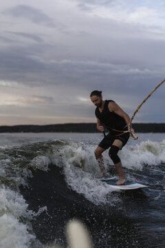 Man wakesurfing on a board in the lake  behind the boat during sunset