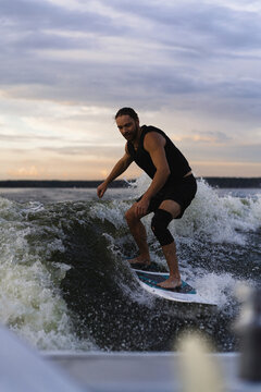 Man wakesurfing on a board in the lake  behind the boat during sunset