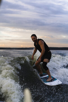 Man wakesurfing on a board in the lake  behind the boat during sunset