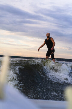 Man wakesurfing on a board in the lake  behind the boat during sunset