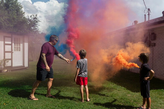 Man and two kids playing with colored smoke bombs outside