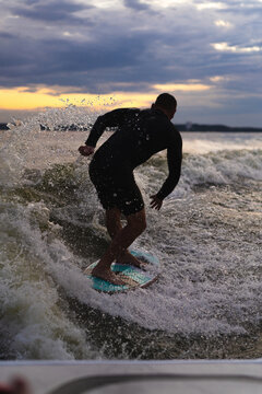 Man wakesurfing on a board in the lake  behind the boat during sunset