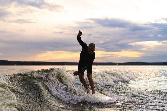 Man wakesurfing on a board in the lake  behind the boat during sunset