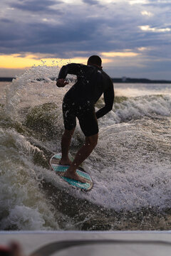 Man wakesurfing on a board in the lake  behind the boat during sunset