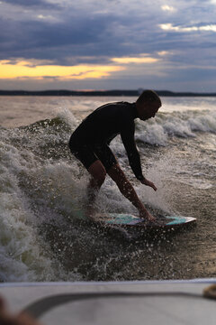 Man wakesurfing on a board in the lake  behind the boat during sunset