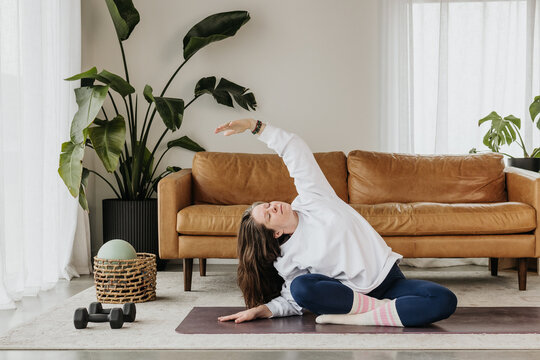 Woman stretches while sitting on her yoga mat in living room
