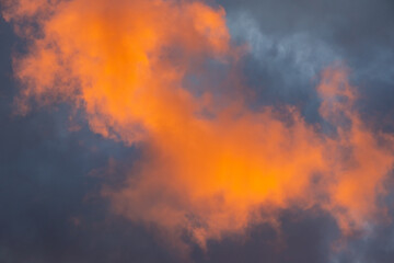 Bright orange clouds illuminated by the setting sun against a dark evening sky