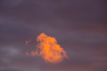 Bright orange clouds illuminated by the setting sun against a dark evening sky