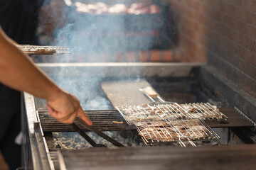 Chef grilling meat on barbecue using tongs in restaurant kitchen