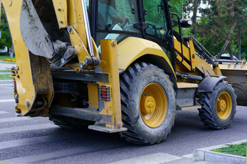 Excavator working on a road repair project near a city park during the morning hours