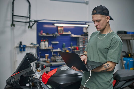 Mechanic in garage using laptop to service motorcycle