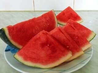 Several slices of ripe watermelon. The slices have bright red juicy flesh and a green rind with a white layer. Some slices have already been separated from the main part of the watermelon and are neat