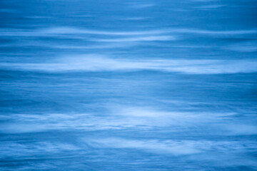 Obraz premium Blurred motion of gentle waves captured with a long exposure, producing a smooth and dreamy blue seascape