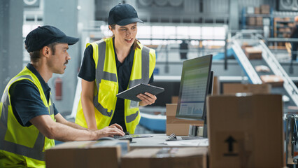 Caucasian Male Stocking Associate Using Desktop Computer, Talking to Female Manager With Tablet In Warehouse Facility With Conveyor Belt. Man And Woman Working In Sorting Center of Online Marketplace.
