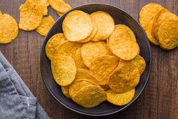 Crispy potato chips in bowl on wooden table. Top view.