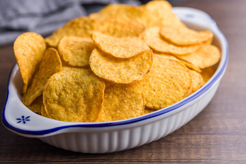 Crispy potato chips in bowl on wooden table.