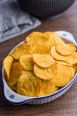 Crispy potato chips in bowl on wooden table.
