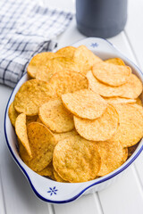 Crispy potato chips in bowl on white table.
