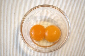 A close-up view of two raw egg yolks inside a transparent glass bowl. Ideal for cooking or food...