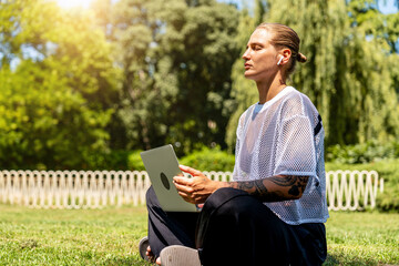 Young modern woman taking a mindful work break while sitting with laptop in city park