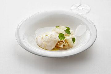 A fine dining dish with fresh pasta, a creamy cheese ball, and delicate herbs, drizzled with olive oil, served in a minimalist white bowl.