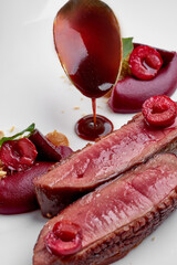 A gourmet dish of perfectly cooked duck breast with cherries, a rich sauce, and crumble, paired with a glass of red wine in the foreground.