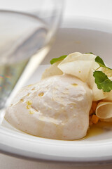A fine dining dish with fresh pasta, a creamy cheese ball, and delicate herbs, drizzled with olive oil, served in a minimalist white bowl.