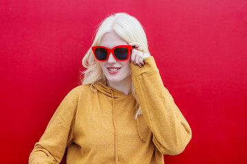 Albinism in fashion: woman with red sunglasses against a vibrant red background