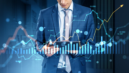 Businessman analyzing financial data on tablet with stock market graphs and currency charts overlayed on digital hologram background concept.
