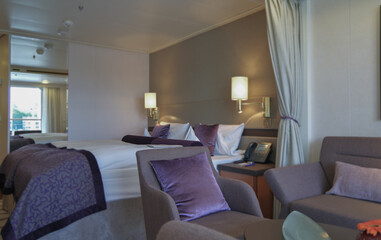 Luxurious suite stateroom cabin room onboard luxury yacht cruise ship cruiseship liner with bedroom and living area in purple and creme with wood in modern Art Deco interior design