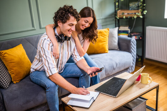 Adult couple is sitting at sofa at home and using laptop.  They are shopping online and making shopping list.
