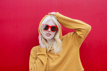 Albino woman posing in a yellow hoodie against a red background