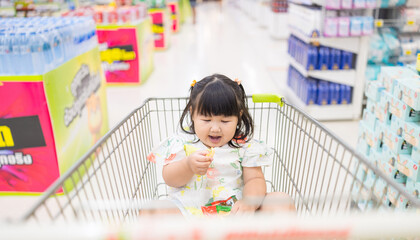 A girl is sitting on a shopping cart in a shopping mall,A cute, bored little girl is sitting on a...