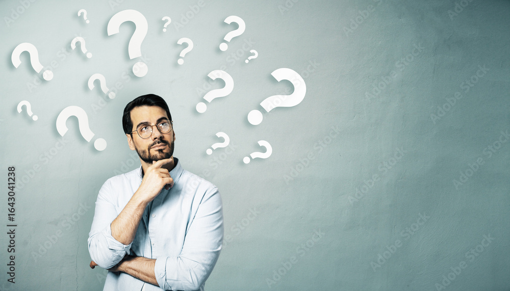 Poster thoughtful businessman standing in front of a wall with floating question marks, symbolizing decisio