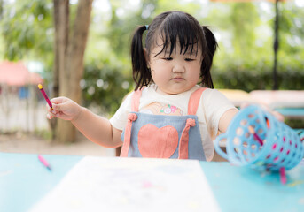 A cute little girl is sitting happily coloring,Asian girl happily drawing with crayons
