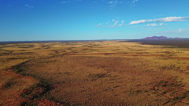 Aerial view of the vast, arid Australian outback, showcasing contrasting red earth meeting the clear blue sky, Ayers Rock, Northern Territory, Australia.