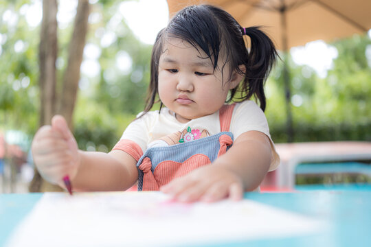A cute little girl is sitting happily coloring,Asian girl happily drawing with crayons
