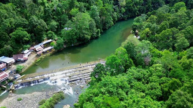 Natural River Cascade Surrounded by Lush Jungle and Riverside Buildings in Sumatera