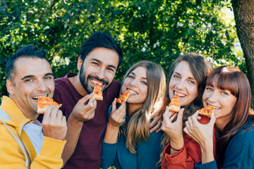 Cheerful friends enjoying pizza outdoors in a park