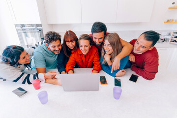 Friends watching laptop in kitchen, sharing funny moment