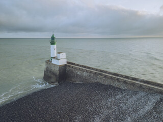 Aerial view of a striking lighthouse with a green top standing guard over the endless sea, where the dark shore meets the horizon, Le TrÃ©port, Normandy, France.