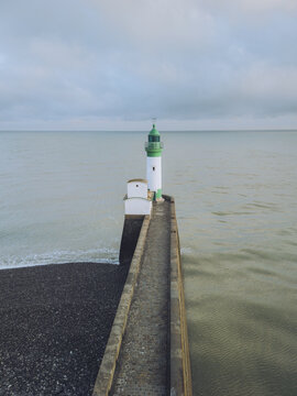 Aerial view of a striking green and white lighthouse standing tall against the muted, calm sea, its beacon piercing the soft, overcast sky, Le Tr&Atilde;&copy;port, Normandy, France.