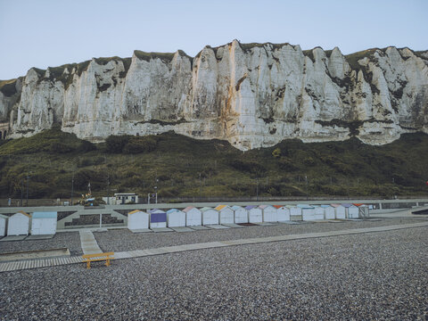 Aerial view of chalk cliffs rise dramatically above a row of colorful beach huts nestled along the pebble beach, Le Tr&Atilde;&copy;port, Normandy, France.