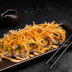 Delicious sushi rolls topped with crispy fried onions served on a dark plate