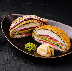 Sushi roll with colorful fillings served on a black plate garnished with wasabi