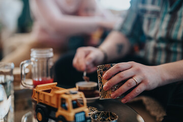 A detailed view of a hand holding an artistic box, with a toy truck and beverages on a table,...