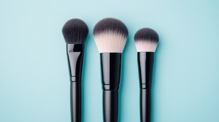 A trio of makeup brushes placed elegantly on a light blue background, showcasing various sizes and shapes, Ideal for beauty blogs, tutorials, or product advertisements