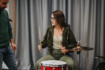 A young woman practices drumming in a music studio setting under guidance.