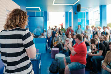 Speaker presenting to a gathered audience in bright tech-themed venue with blue decor.