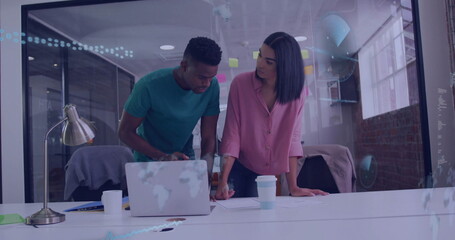 Professionals leaning over conference table in office with laptop, coffee cup, sticky notes